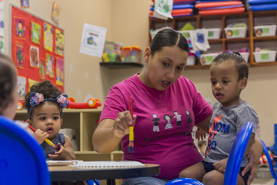 child care teacher works with young boy in a classroom.