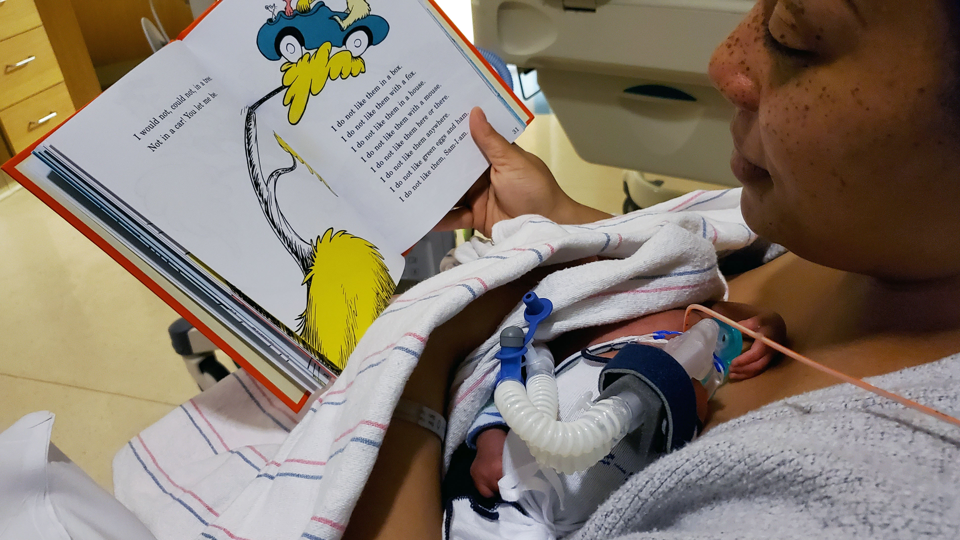 Parent reading book to newborn in NICU unit