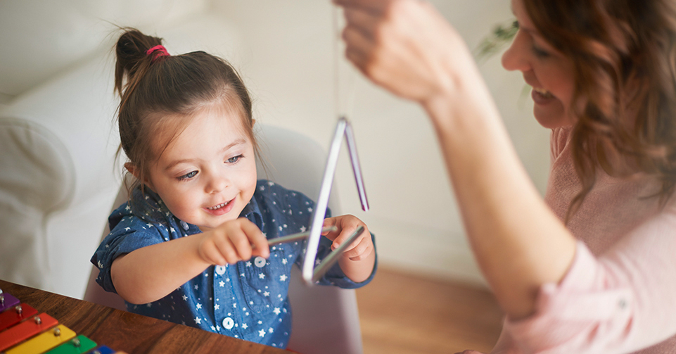 small girl playing with triangle musical instrument