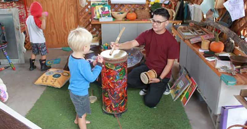 male pre-k teacher playing a drum with a young boy.g