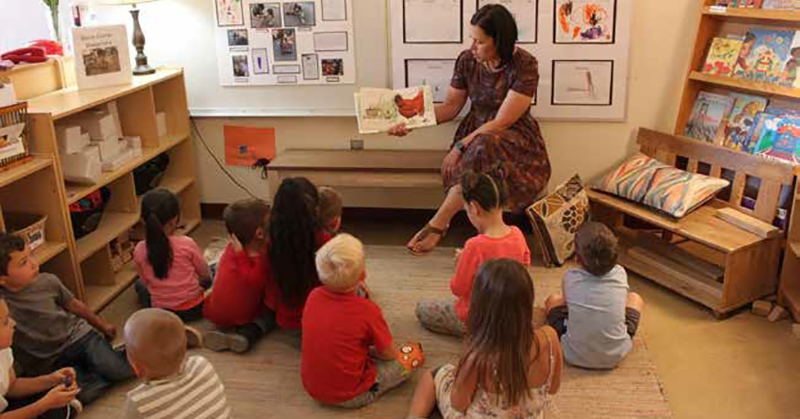 preschool teacher reading a book to a group of children