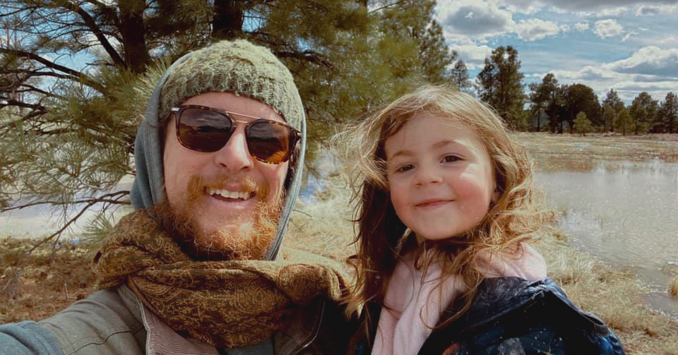 father in beanie wearing sunglasses with daughter who is smiling and wearing a denim jacket