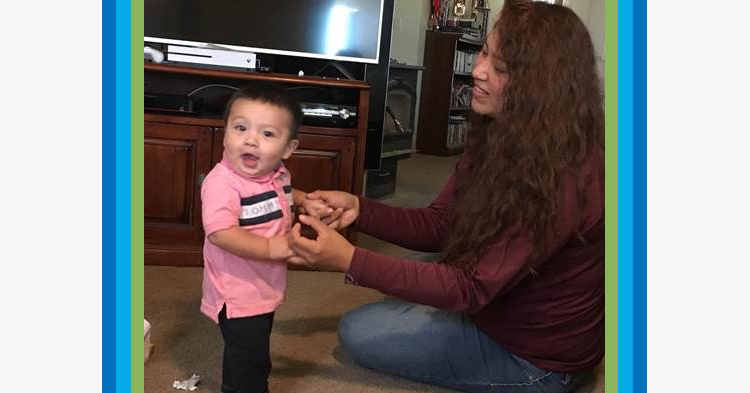 Mom holding her sons hands as he learns how to walk