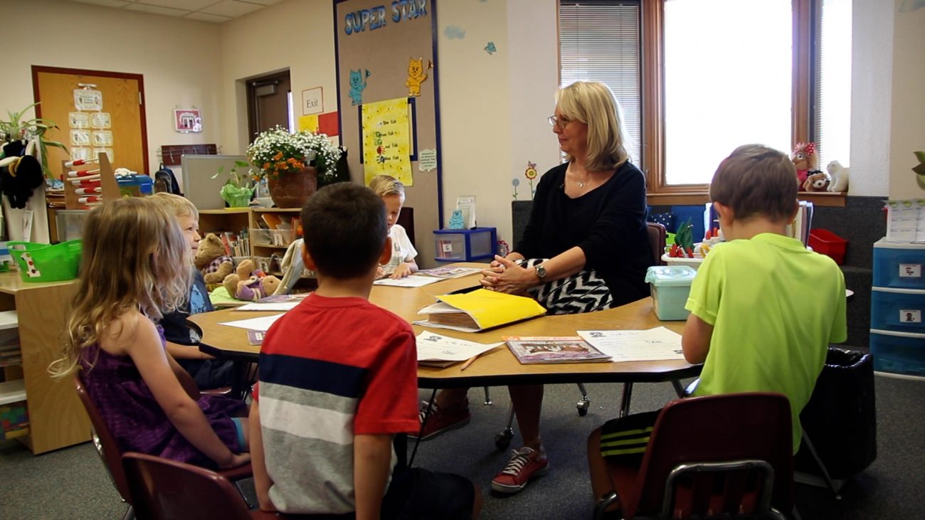 kindergarten teacher sitting at a table with students.