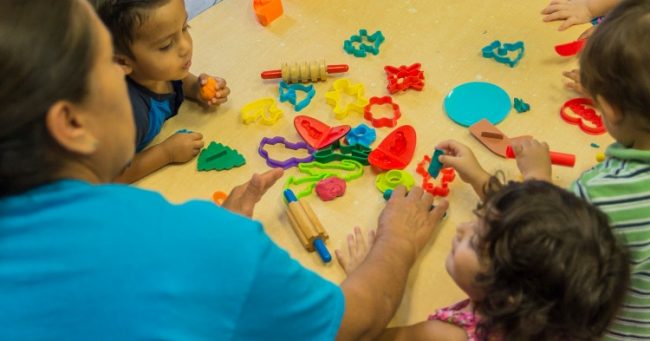 teacher and preschoolers around a table with play dough and cutters
