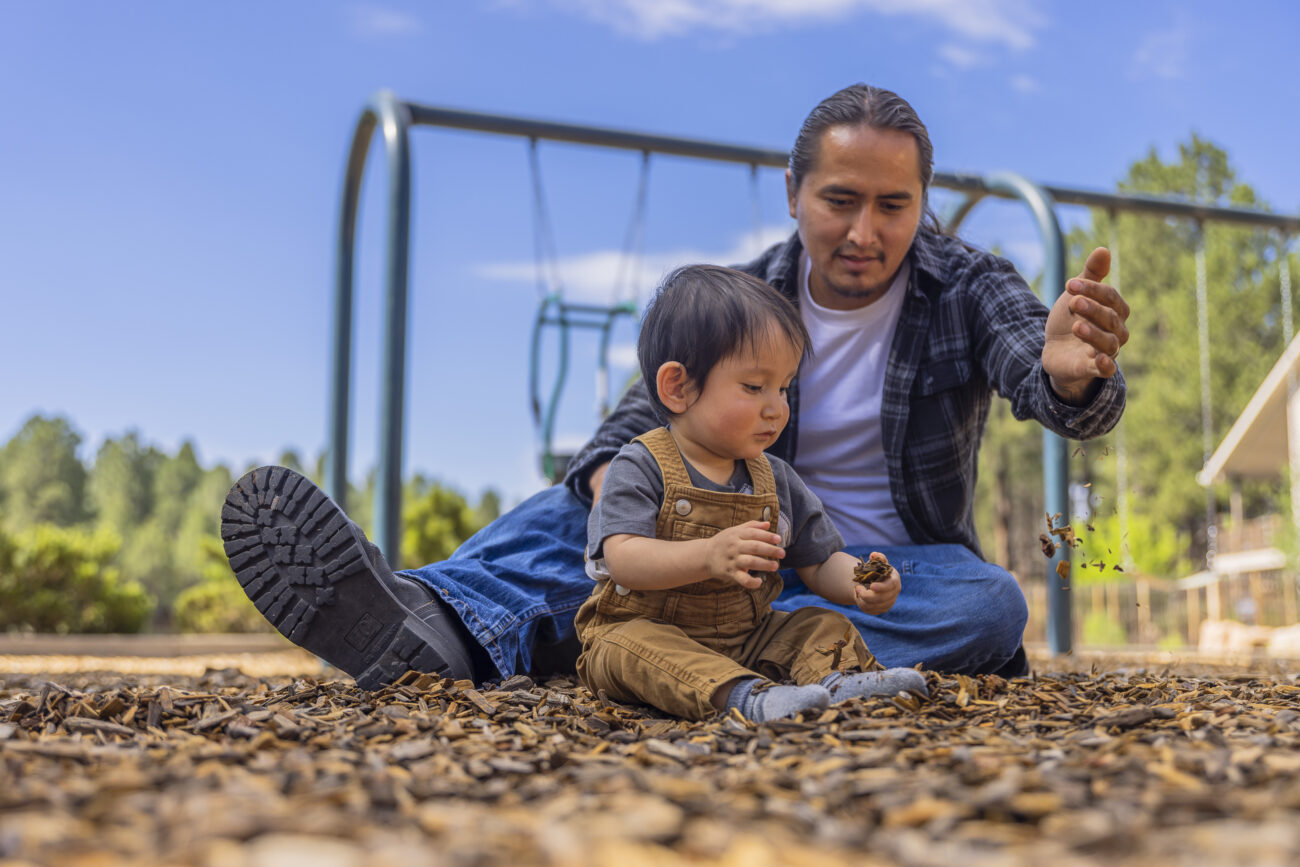 Dad and baby son playing in park on the floor with leaves.