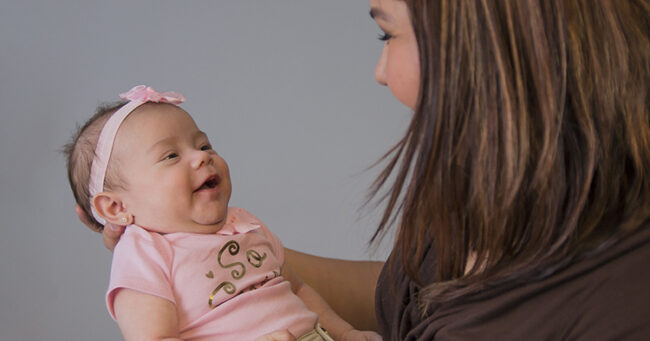 Mom hold small baby, who is wearing a pink bow on her head.